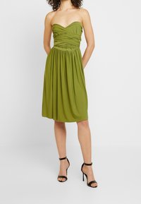 Robe bustier verte olive avec texture froncée au corsage et jupe fluide. Finition en tissu lisse avec un design plissé.
