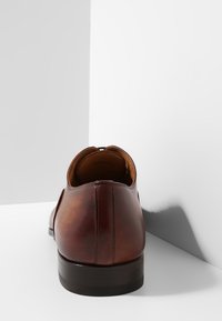 Chaussure habillée en cuir marron avec une texture lisse, un talon arrondi et une silhouette élégante, présentant des détails de couture subtils et une finition polie.