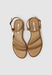 Sandalias de ante marrón con tres tiras delgadas y una correa al tobillo. Plantilla suave en beige y suela lisa. Diseño elegante y minimalista.