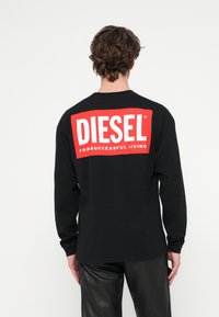 Melnas krāsas T-krekls ar garām piedurknēm, uz muguras lielā sarkana "DIESEL" logo un teksts "FOR SUCCESSFUL LIVING". Klasiska piegriezuma, kokvilnas materiāls.