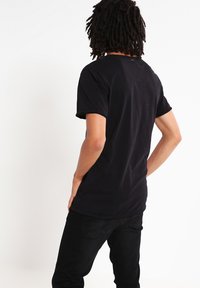 Zwart katoenen T-shirt met korte mouwen, ronde hals en een minimalistisch ontwerp, gecombineerd met zwarte jeans, gezien van de achterkant.