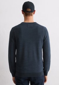 Granatowy dzianinowy sweter z długimi rękawami, okrągłym dekoltem i teksturowaną tkaniną. Posiada wąski prążkowany dół i mankiety, noszony z ciemną czapką.