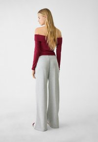 Off-the-shoulder maroon top parret med lysegrå, brede bukser. Toppen har lange ærmer; bukserne har en afslappet pasform og blød tekstur.
