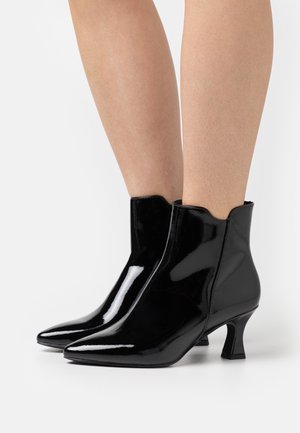 Bottines noires en cuir verni avec un bout pointu, un bord supérieur à bords festonnés et un petit talon épais. Fini lisse et brillant.