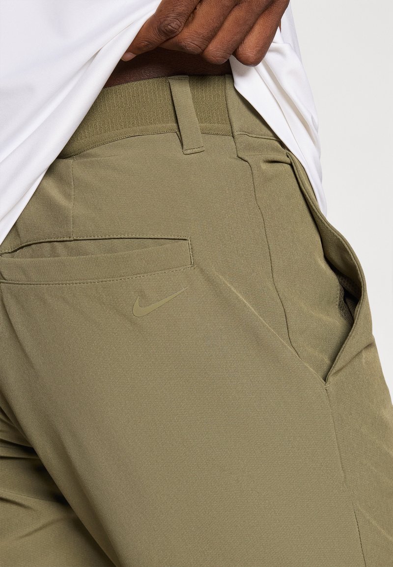 Olijfgroene Nike-broek met een gladde, gestructureerde stof, elastische tailleband, zijzakken en een klein logo op het linkerbeen.