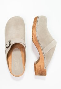 Beige Wildlederschuhe mit einem Holzabsatz, ausgestattet mit einem breiten Riemen und einer Metallschnalle sowie einer strukturierten Außensohle.