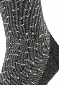 Schwarz-weiße Socken mit geometrischem Muster. Stricktextur mit weißen Akzenten. Verstärkter Fersenbereich für Haltbarkeit.