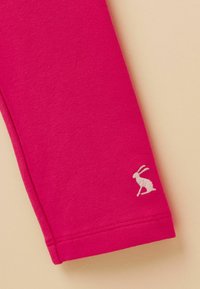 Manchon en tissu rose vif avec un petit lapin blanc brodé près de l'ourlet sur un fond beige.