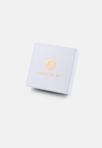 Caixa de presente texturizada branca com um logotipo em relevo dourado e o nome da marca "GINETTE NY" na parte da frente, apresentando um formato quadrado e um design limpo.