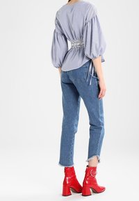 Randig blus med puffärmar och insydd midja; kombinerad med ljusblå jeans och glänsande röda anklarstövlar med klackar och ringdetaljer.