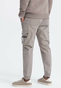 Grå cargobyxor med sidofickor, dragkedjedetaljer och avsmalnande ben, tillsammans med beige sneakers. Tyget verkar hållbart och texturerat.