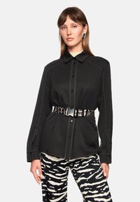Black button-up shirt with contrasting white stitching, paired with zebra-patterned pants and a patterned belt. Long sleeves and collared design.