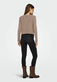 Top marrón con textura de canalé y manga larga, combinado con jeans ajustados negros y botines de ante marrón con hebilla. Vista trasera que muestra la textura y el ajuste de la tela.