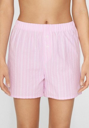 Mujer con pantalones cortos de algodón a rayas rosas y blancas con cintura elástica y dos pequeños botones delanteros, con las manos relajadas a los lados.