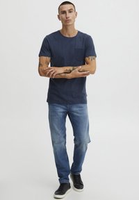 Marineblå t-skjorte med lomme, kombinert med lys blå jeans og svarte joggesko. Stoffet ser glatt ut med en avslappet passform.