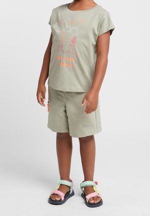 Olivově zelené tričko s grafickým designem a odpovídajícími šortkami. Obuv: vícebarevné sandály s růžovými, zelenými a žlutými akcenty.