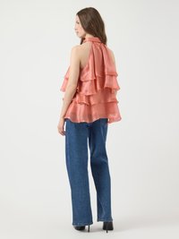 Top halter in satin pesca con rouches a strati; abbinato a jeans in denim blu a gamba larga e tacchi neri. Tessuto liscio, leggero.