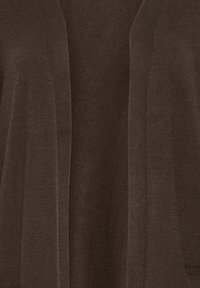 Gros plan d’un cardigan tricoté marron à ouverture devant montrant la texture et les détails nervurés verticaux le long des bords.