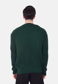 Maglione verde lavorato a maglia con un motivo a coste testurizzato, maniche lunghe, scollo rotondo e spacchi laterali all'orlo.
