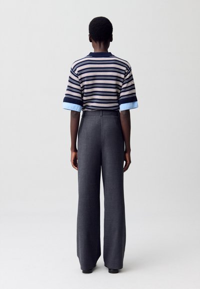 Camisa de manga corta a rayas en azul marino y crema con puños azules, combinada con pantalones de pierna ancha grises de cintura alta. Textura de tela suave.