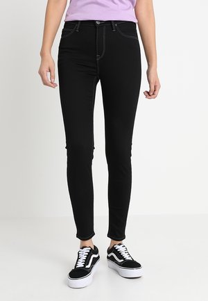 Jeans skinny negros de denim, con costuras blancas en contraste, cierre frontal con botón y un diseño clásico de cinco bolsillos.