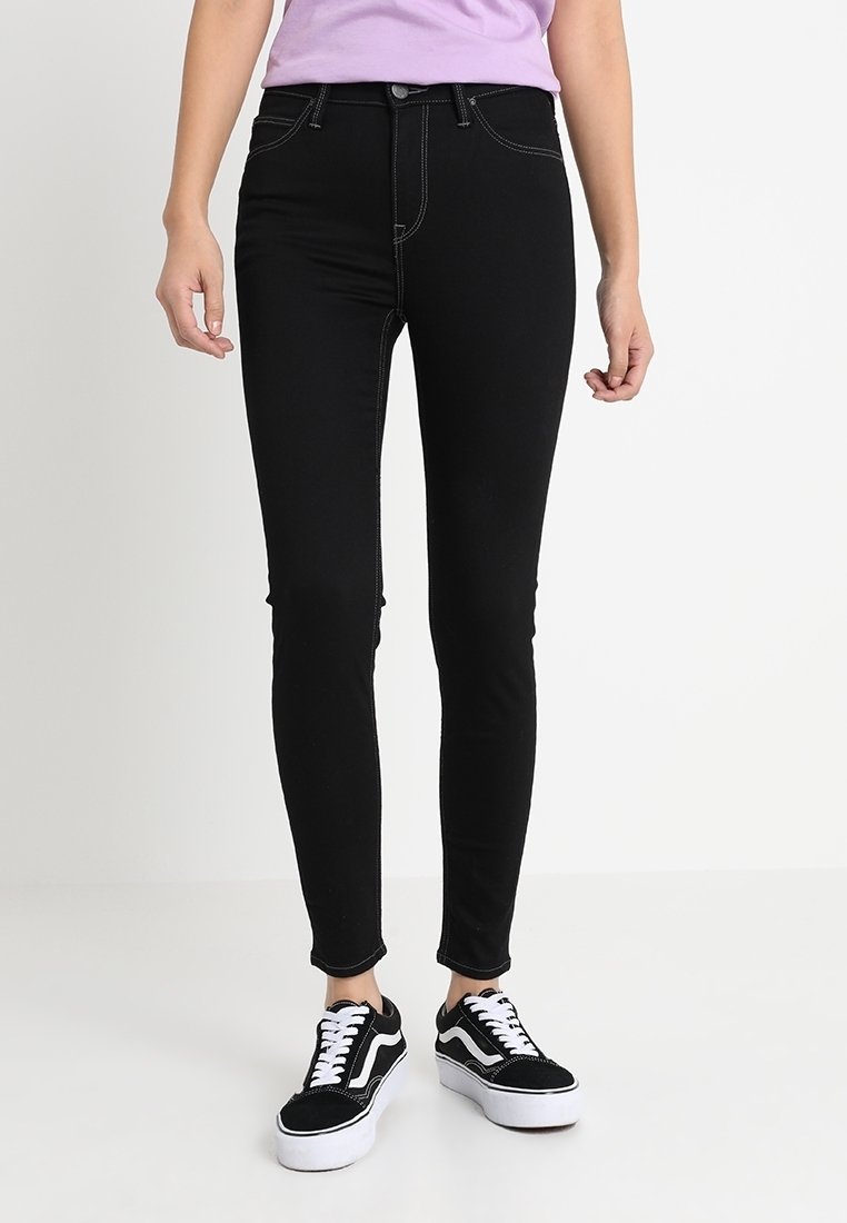 Jeans skinny negros de denim, con costuras blancas en contraste, cierre frontal con botón y un diseño clásico de cinco bolsillos.