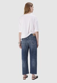 Witte oversized t-shirt met korte mouwen, gecombineerd met relaxed-fit, vervaagde blauwe denim jeans. Beschikt over een lichte drop hem en achterzakken.