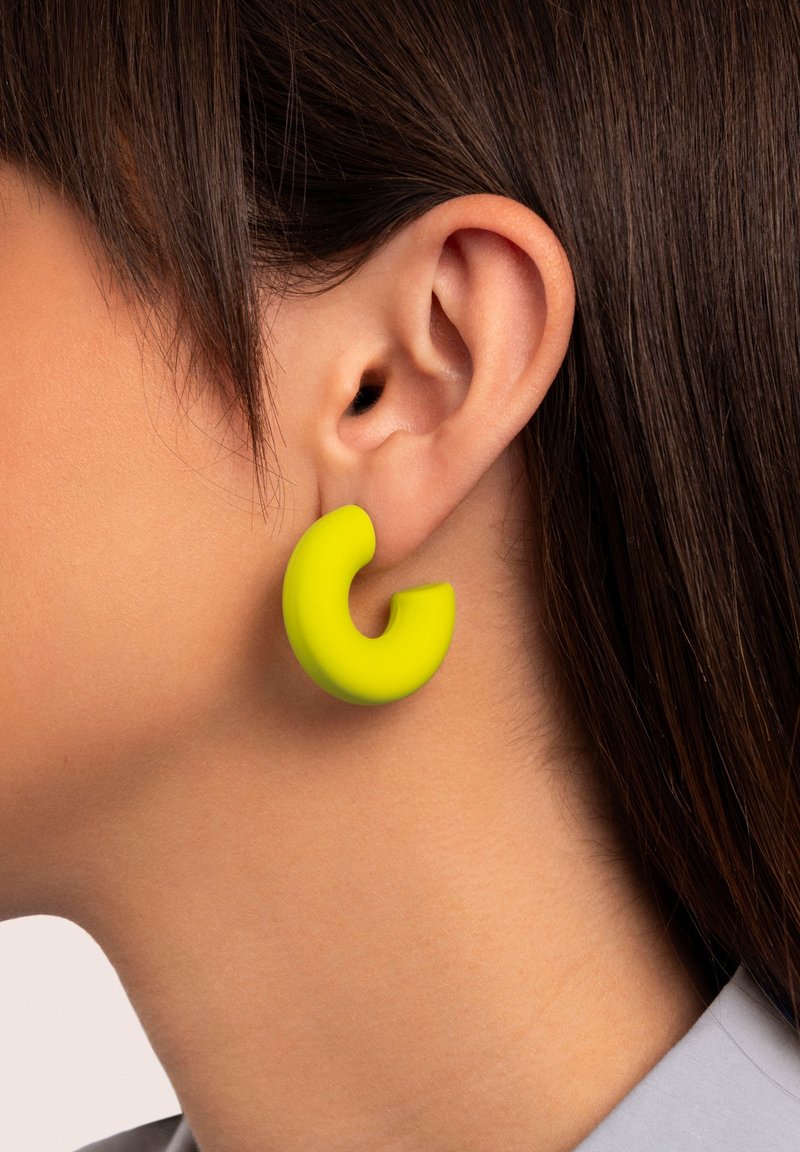 Boucles d'oreilles circulaires de couleur jaune vif, finition mate, avec un design découpé. Mettez l'accent sur la forme unique, la texture et le contraste de couleur audacieux contre la peau.