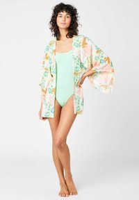 Kimono floral con patrones vibrantes en naranja, rosa y verde; mangas sueltas; tejido ligero; combinado con un traje de baño verde menta.