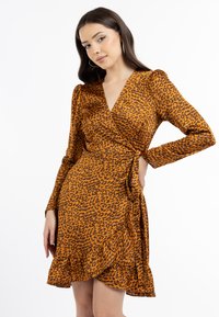 Leopardikuvioinen kietaisumekko oranssina ja ruskeana, valmistettu pehmeästä kankaasta. Ominaisuuksiin kuuluvat pitkät hihat ja röyhelöhelmassa.