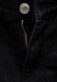 Gros plan sur un tissu noir avec une fermeture éclair en laiton ouverte et un bouton argenté sur un jean ou un pantalon.