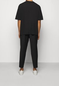 Mustat ylisuurikokoiset t-paita ja siihen sopivat housut, molemmat pehmeästä kankaasta. T-paidassa on pyöreä kaula-aukkko. Valkoiset tennarit täydentävät asun.