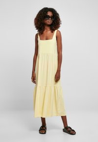 Geel, mouwloze maxi-jurk met vierkante halslijn en gelaagde rok. Gemaakt van zachte stof, heeft een ontspannen pasvorm en een vloeiende silhoutte.
