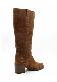 Stivale marrone in suede alto fino al ginocchio con punta quadrata, tacco chunky in legno e una linguetta laterale per facilitare la calzata. Texture liscia con cuciture rinforzate.