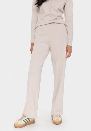 Lichtbeige, loszittende gebreide broek met een wijde pijp, met een zachte textuur. Gecombineerd met casual schoeisel in crème en groen.