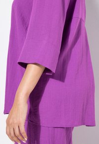 Top viola largo con maniche ampie, tessuto texturizzato e orlo che scende sotto la vita, che mette in mostra un design casual.