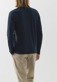 Granatowa koszula z długim rękawem wykonana z gładkiego materiału, charakteryzująca się prostym krojem i okrągłym dekoltem, zestawiona z jasnobeżowymi spodniami.