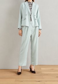 Vaaleansininen räätälöity bleiseri, jossa on kaksiriviset napit, yhdistettynä väljiin, samaa materiaalia oleviin housuihin. Mustavalkoinen kuvioitu yläosa ja mustat korkokengät ilman takakappaletta.