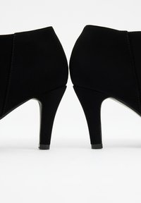 Botines de ante negro de tacón alto con un diseño elegante, punta afilada y una silueta minimalista. Presentan un tacón brillante y costuras sutiles.