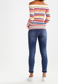 Off-the-shoulder, meerkleurige gestreepte lange mouw top met een strakke pasvorm, gecombineerd met donkerblauwe skinny jeans en witte sneakers.