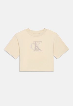 Lyhythihainen, lyhyt t-paita vaaleassa kermanvärisessä kankaassa, jossa on pehmeä tekstuuri, ja jossa on hillityllä muotoilulla brodeerattu 'CK' -logo.