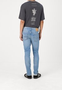 Schwarzes Grafik-T-Shirt mit floralem Design auf dem Rücken, kombiniert mit hellblauen Jeans. Die Jeans haben einen hellbraunen Lederpatch am Bund.