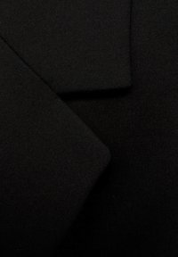 Zwart stof dat een gladde textuur toont; meerdere stukken overlappen elkaar en demonstreren een schone, matte afwerking met scherpe randen en hoeken.