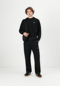 Black crew neck sweatshirt, matching cargo pants, and black sneakers with brown soles. Both garments feature minimal detailing.