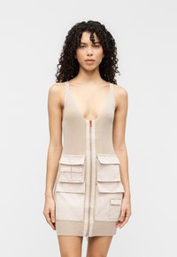 Μπεζ ριγωτό φόρεμα με βαθύ V λαιμόκοψη, φερμουάρ μπροστά και δύο μεγάλες τσέπες στο στήθος. Υφή υφάσματος με λείες λεπτομέρειες στις τσέπες.