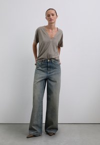 Camiseta beige de cuello en V hecha de una tela suave, combinada con unos jeans anchos de tiro alto en un lavado claro que cuentan con bolsillos frontales y cierre de botón.