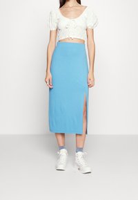 Světle modrá elastická sukně midi délky se skluzem na straně, v kombinaci s bílým topem na krátký rukáv s volnými rukávy a bílými teniskami na vysoké podrážce.