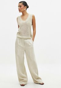 Haut en tricot sans manches beige avec un décolleté arrondi, associé à un pantalon large beige clair, doté de plis sur le devant et d'une finition texturée.