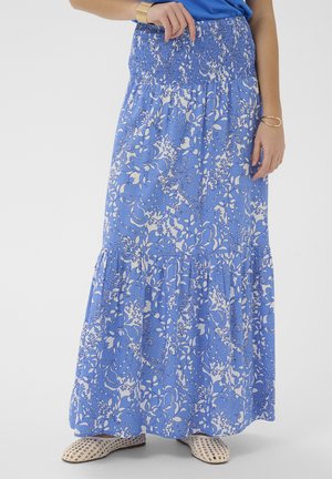 Blue and white floral maxi skirt with smocked waistband, worn with white woven flats and gold bracelet on left wrist.