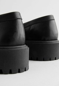 Black leather shoes with a rounded design, featuring a chunky black sole with a serrated edge and smooth finish. Minimal stitching detail.